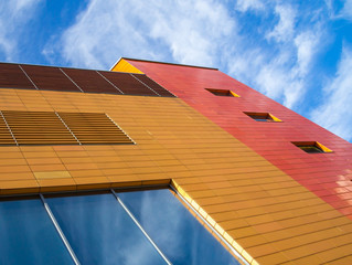 Fragment of the facade of an orange building against a blue sky with white clouds