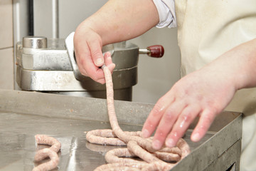 A worker at the meat processing factory, prepares sausages at the work table. Food processing and processing industry. Raw meat mix: steaks, poultry, sausages, ham, chopped, minced meat. The farm