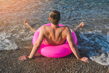 Fototapeta na wymiar Happy man in pink with a big inflatable ring on the sea beach in summer sunny day.