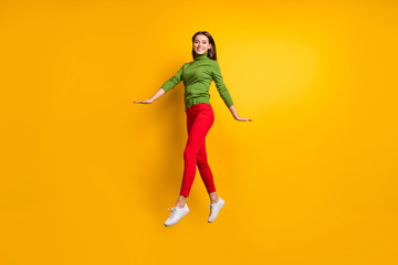 Fototapeta na wymiar Full length photo of beautiful lady jumping high walking down street enjoy warm spring weather wear casual trendy green jumper red pants isolated yellow color background