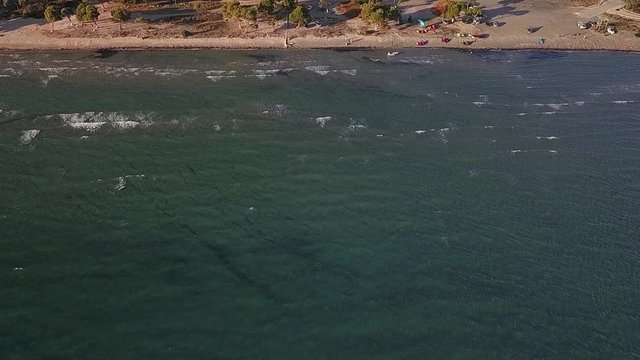 Slow tilt up, reveal drone shot of a beach in Greece with kitsurfers