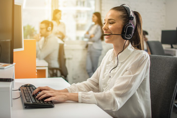 Smiling female helpline operator with headset in call center.