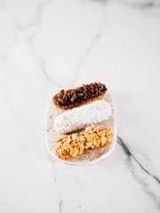 Set of three homemade eclairs on marble background. Top view of delicious healthy profitroles with different decor elements - chocolate, peanut and sherdded coconut. Vertical