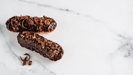 Set of homemade eclairs with chocolate on white marble background. Close up view of delicious healthy profitroles with chocolate glaze. Copy space for text or design. Banner