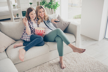 Full body photo of pretty lady mom daughter sit sofa hugging eat popcorn switch on tv set watch favorite comedy stay home quarantine spend time together best friends living room indoors