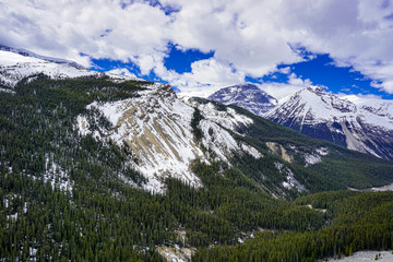 Snowcapped Canada's Rockies mountain during a summer day contrasting with a bright blue sky and white clouds