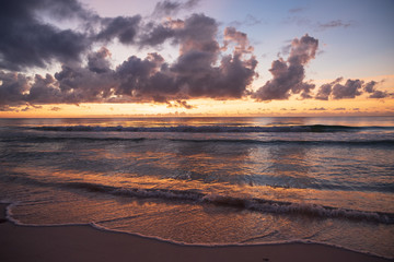 Fototapeta na wymiar Orange sunrise and dramatic sky reflect on the clear waters on a beach near Tulum. Beautiful sunrise Mexican hues. 