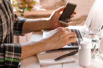 Businessman, freelancer holding pen, using mobile smart phone, working on laptop computer at home