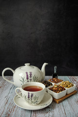 Mug with red tea, teapot and dry tea leaves. Dark background with copy space