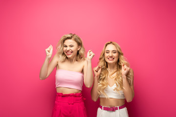Happy blonde women showing yeah gesture on pink background