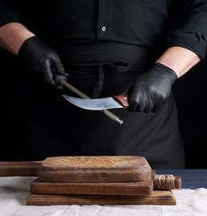 chef in a black shirt and black latex gloves sharpen a kitchen knife on an iron sharpener with a handle