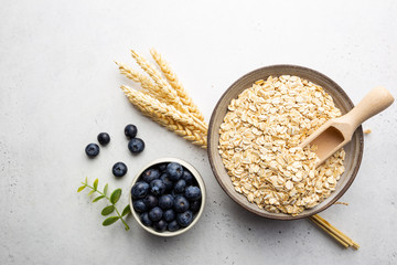 Rolled oats or oat flakes in bowl and wooden spoon on white table, top view with copy space