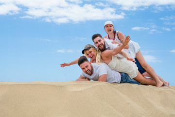 Four happy friends playing and fooling around together on the sand dunes of the beach.