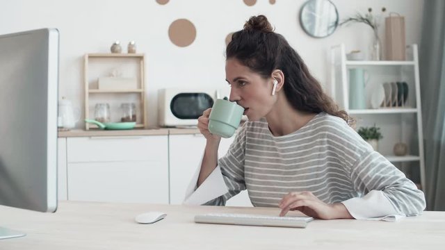 Time lapse of pretty female freelancer wearing wireless headphones sitting at table in front of computer, consulting client remotely and coking lunch