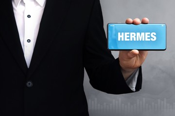 HERMES. Geschäftsmann im Anzug hält ein Smartphone in die Kamera. Der Begriff HERMES steht auf...