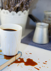Coffee spilled on a book on the desktop. A cezve for coffee, coffee beans, a white cup of coffee, spill a drink on the table, making a puddle and ruining the book. Kitchen table, cook.