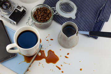 Coffee spilled on a book on the desktop. A cezve for coffee, coffee beans, a white cup of coffee, spill a drink on the table, making a puddle and ruining the book. Kitchen table, cook.