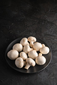 Champignon mushrooms healthy food on black plate on dark black textured background, angle view copy space