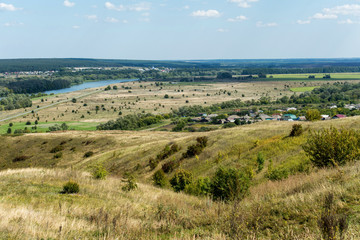 Obraz premium Rural landscape with rustic homes, fields of wheat, sheafs and river