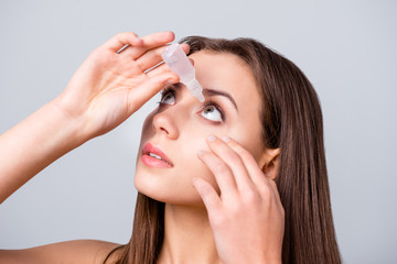 Close-up portrait of her she nice attractive lovely pretty brown-haired girl applying eye drops prescription medication isolated over grey pastel color background