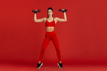 Fototapeta na wymiar Confidence. Beautiful young female athlete practicing in studio, monochrome red portrait. Sportive fit brunette model with weights. Body building, healthy lifestyle, beauty and action concept.