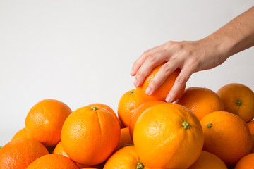 Person taking orange from fruits heap isolated on white background. Closeup shot, side view. Healthy nutrition or organic food concept