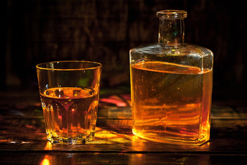 A glass of alcohol near a bottle. Old whiskey bottle on black wooden table. Drinks on a dark blurred background.