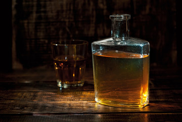 A glass of alcohol near a bottle. Old whiskey bottle on black wooden table. Drinks on a dark blurred background.