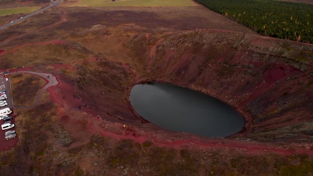 Aerial 4k view of an Icelandic crater lake on top of Kerio Volcano with tourists walking on top of it, orbit right shot