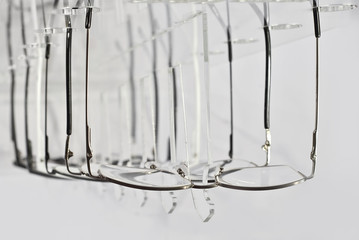 Many glasses on a white background. Glasses are stacked in a row on a transparent shop window. Glass stand on gray table. Sale and exhibition of optics.