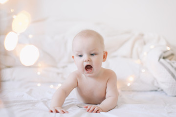 Little child doing tummy time. Adorable baby learning to crawl in white  bedroom. Cute funny baby lying on bed. 