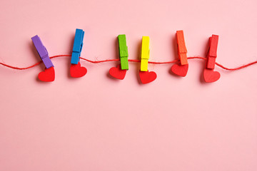rainbow colored wooden clothespins with clamped red hearts on pink background. Pride day concept, flat lay, copy space