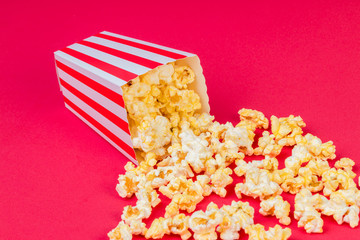 Paper cup with popcorn on color background. Striped box with popcorn on red background.Popcorn in red and white striped cardboard bucket .