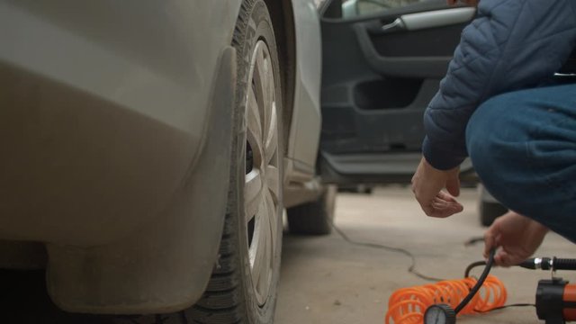 Close up of male hands screwing a car pump to a tire valve of back wheel of a car. Vehicle auto maintenance