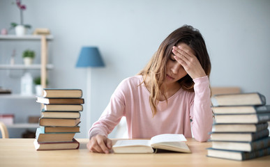 Sad female student reading a book for the exam or doing homework.
