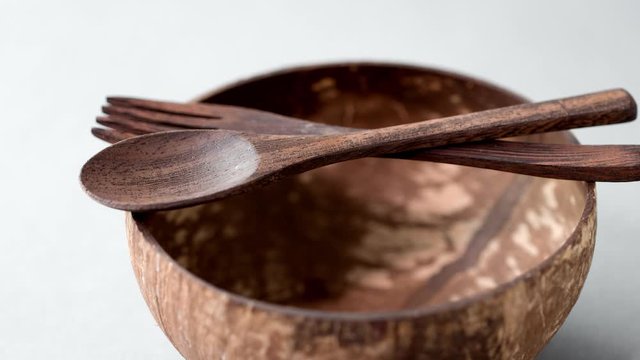recycling, tableware and eco friendly concept - close up of coconut bowl with brown wooden spoon and fork on table