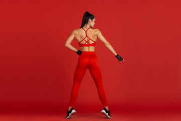 Fototapeta na wymiar Ideal body. Beautiful young female athlete practicing in studio, monochrome red portrait. Sportive fit brunette model training. Body building, healthy lifestyle, beauty and action concept.