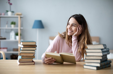 Portrait of young happy woman sits at a table with books studying at home.