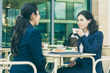 Businesswomen drinking coffee in outdoor cafe. Female colleagues in formal wear sitting at table and drinking coffee together. Coffee time concept