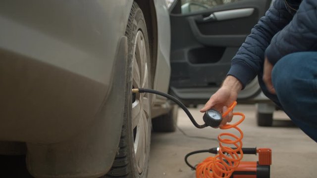 Close up of man holding a manometer in his hand while a pump inflates a car wheel. Vehicle auto maintenance