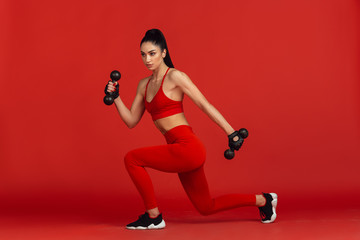 Graceful. Beautiful young female athlete practicing in studio, monochrome red portrait. Sportive fit brunette model with weights. Body building, healthy lifestyle, beauty and action concept.