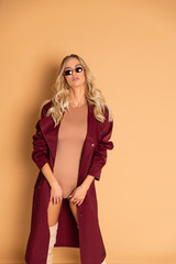 Sexy Blonde model with perfect skinny body with huge boobs posing in beige combidress and glam red coat so good fashion style retouched in very high quality