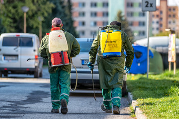 Professionals in protective suit disinfects with a sprayer in the city.