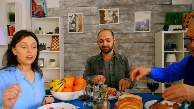 Man in his sixties serving his wife with bread at family dinner.