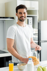 Fototapeta na wymiar Selective focus of smiling man holding cereals near orange juice and apples on kitchen table