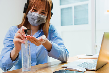 Asian young business woman wearing face mask protective working from home office with laptop computer he quarantines disease coronavirus or COVID-19 and cleaning hands with sanitizer alcohol gel pump