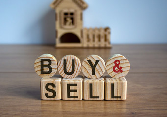 Cubes and circles form the words 'buy sell' in front of a miniature house.