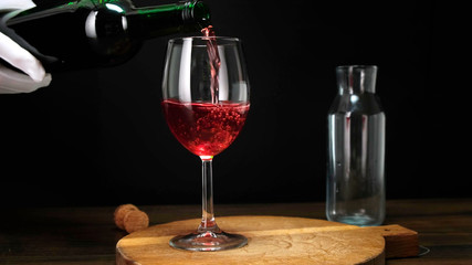 Skilled sommelier pouring red wine from bottle into Glass. Close up.