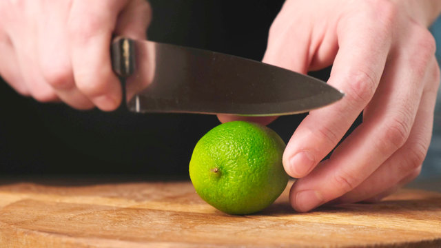 Sliced in half fresh lime with knife on wooden chopping board. Close up.
