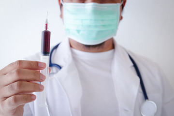 The doctor wears a medical mask and holds a syringe containing the patient's blood to check for epidemics. Treatment hospital concept